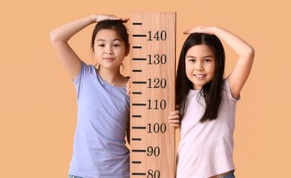 two children stand either side of a height chart